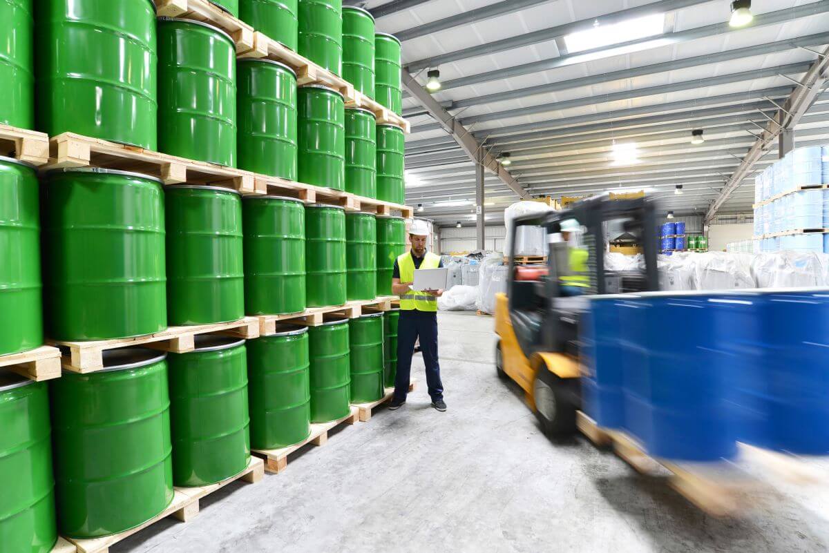 A worker and a truck among green barrels